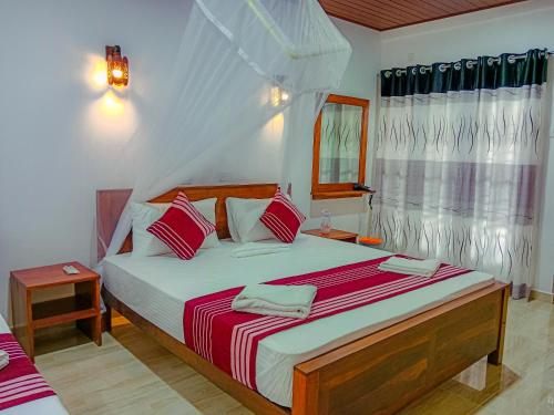 a bedroom with a large bed with red and white sheets at Sigiriya Peacock Homestay in Sigiriya