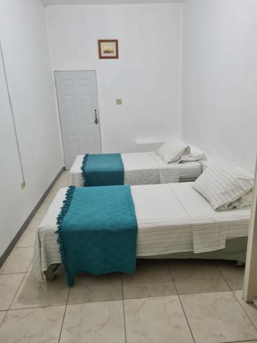two beds in a white room with blue sheets at La Rose Apartment in Montego Bay