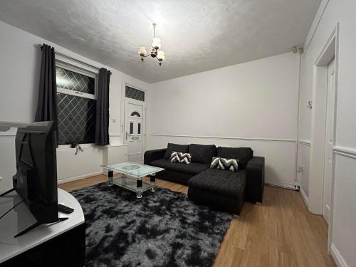 a living room with a black couch and a tv at Comfortable, spacious 2 Bedroom house close to Etihad Stadium in Stalybridge