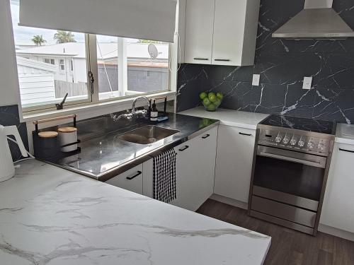 a kitchen with white cabinets and a sink and a window at Omanu Cottage in Mount Maunganui