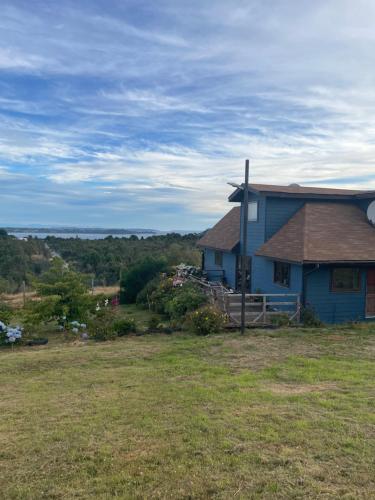 a blue house on top of a grass field at Casa Sra Oti, Tipo Hostal con vista al mar Puerto Montt - CHINQUIHUE in Puerto Montt