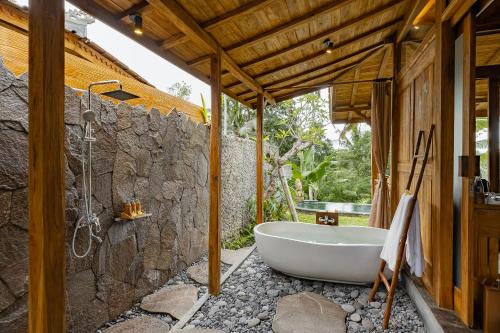 a bathroom with a tub and a stone wall at Anandari Ubud Villa in Ubud