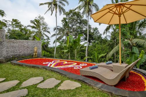 a garden with a table and an umbrella and red flowers at Anandari Ubud Villa in Ubud