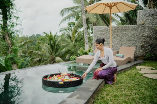 a woman sitting next to a pool with a bowl of fruit at Anandari Ubud Villa in Ubud