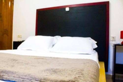 a bed with a black headboard and white pillows at Résidence OSTHOME in Douala