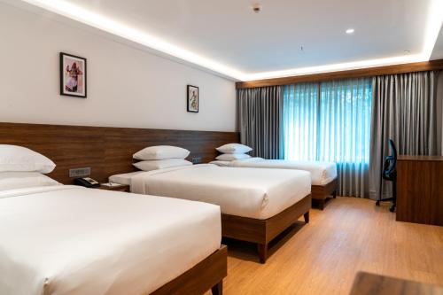 a hotel room with three beds and a window at Lilac Hotel Guruvayur in Guruvāyūr