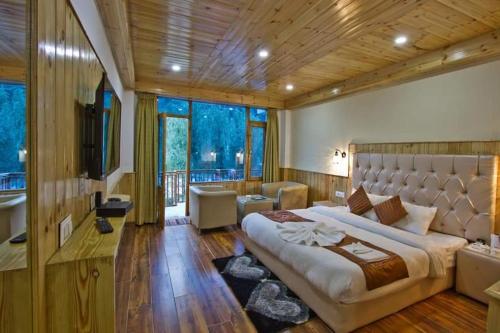 a bedroom with a large bed and a large window at Himalayan Riverside Resort, Manali in Manāli