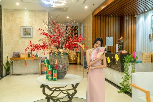 Una mujer con un vestido rosa parada en el vestíbulo en Star City Riverside Hotel By Haviland, en Da Nang