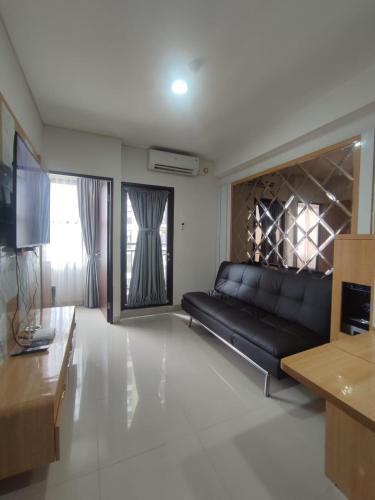 ein Wohnzimmer mit einem schwarzen Sofa und einem TV in der Unterkunft Apartment TransPark Cibubur, TSM in Kalimanggis