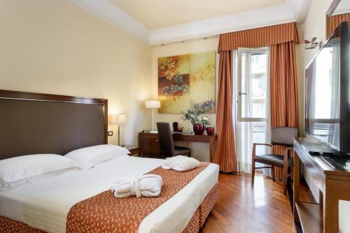 フィレンツェにあるグランド ホテル アドリアティコのベッドとデスクが備わるホテルルームです。