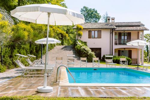 una casa y una piscina con sombrilla y sillas en La Panoramica Da Stroppa, en Acqualagna