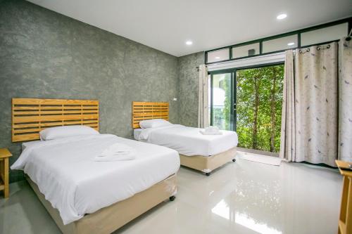 twee bedden in een kamer met een groot raam bij บ้านเราอุทัยธานี โฮมสเตย์ in Uthai Thani