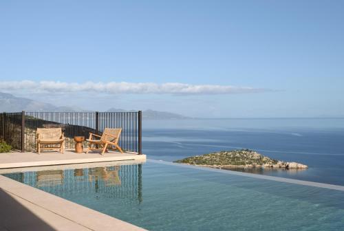 a swimming pool with two chairs and a view of the water at Verdante Villas in Agios Nikolaos