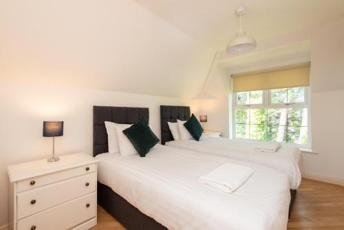 two white beds in a bedroom with a nightstand and a window at The Pines in Middlesbrough