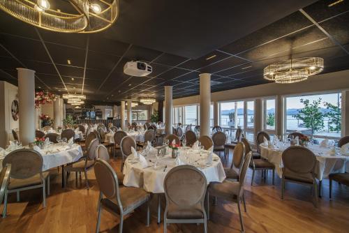 um salão de banquetes com mesas e cadeiras brancas e janelas em Molde Fjordhotell - by Classic Norway Hotels em Molde