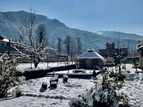 a yard covered in snow with a building and mountains at Flüstern Manali in Nagar