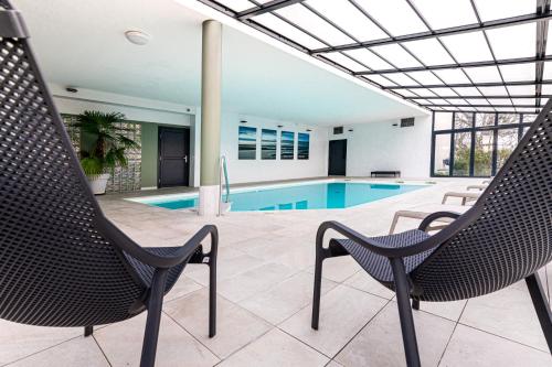 a pool with two chairs and a swimming pool at Kyriad Prestige Residence & Spa Cabourg-Dives-sur-Mer in Dives-sur-Mer