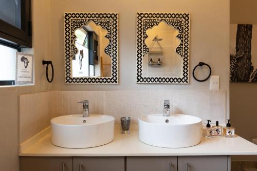 a bathroom with two sinks and two mirrors at Africa House in Hoedspruit