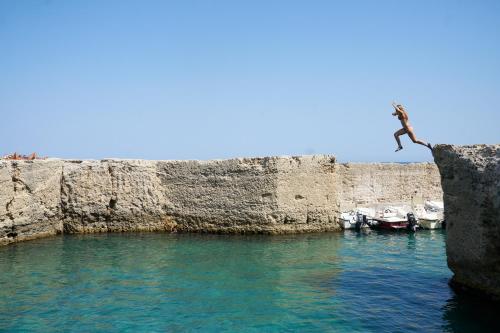a person jumping off a cliff into the water at Il Cubetto- a cute mini house in olive grove in Surano