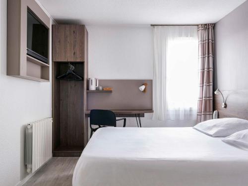 MassieuxにあるHOTEL Lyon Nord Massieux Genayのベッドとデスクが備わるホテルルームです。