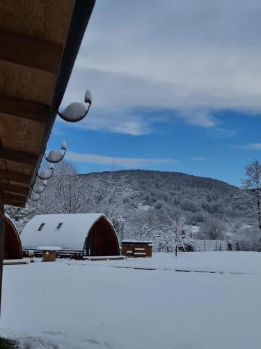a snow covered field with a barn and a mountain at Căsuțe în mijlocul naturii - Wild Camp Avrig in Avrig