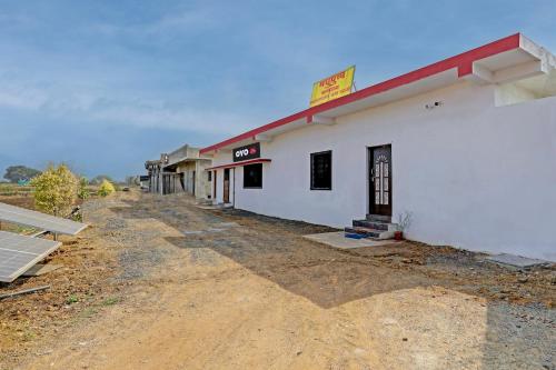 een wit gebouw met een rood dak op een onverharde weg bij OYO Madhupushpa Farm House in Rāmtek
