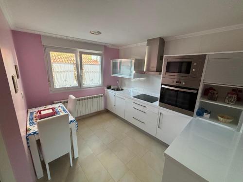cocina con paredes de color rosa, armarios blancos y mesa en Casa Lalo, en Camariñas