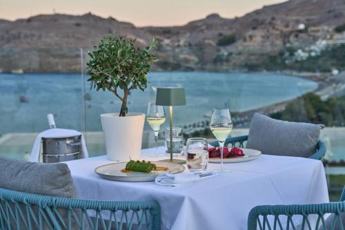 a table with glasses of wine and a tree on it at Lindos Grand Resort & Spa - Adults Only in Líndos