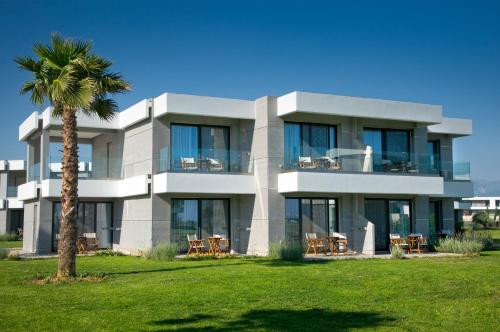 a white building with a palm tree in front of it at Neilson Messini Activity Beach Club in Kalamata