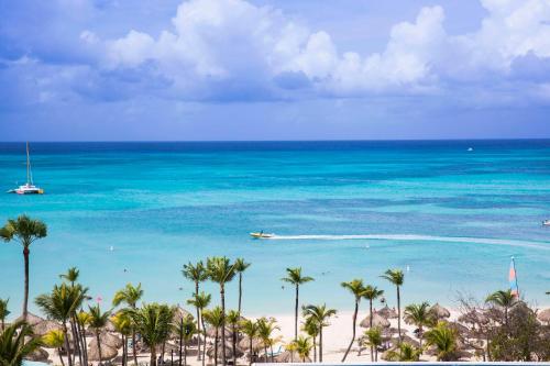 a beach with palm trees and a boat in the water at Hilton Aruba Caribbean Resort & Casino in Palm-Eagle Beach