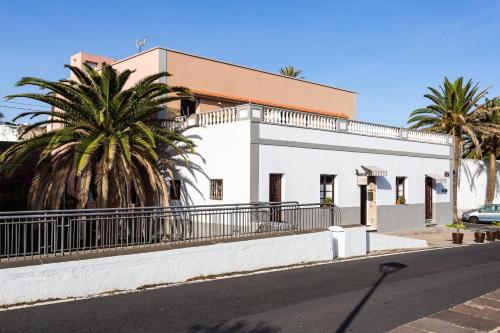 a white building with palm trees next to a street at El Hostal del Cubo in San Juan de la Rambla