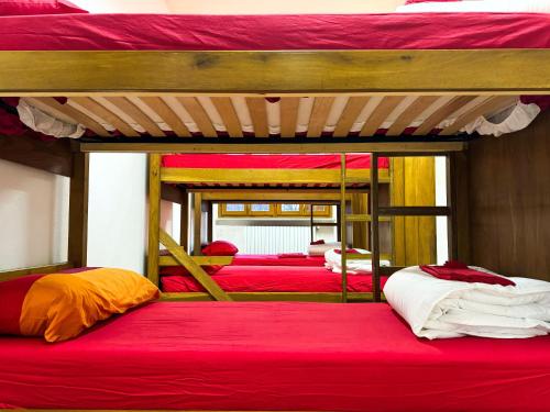 three bunk beds in a room with red sheets at Rifugio Nido del Biancone in Bosio