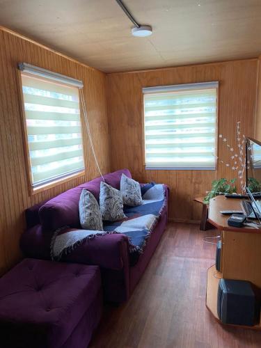 sala de estar con sofá púrpura y 2 ventanas en Cabaña centro Frutillar Alto, en Llanquihue