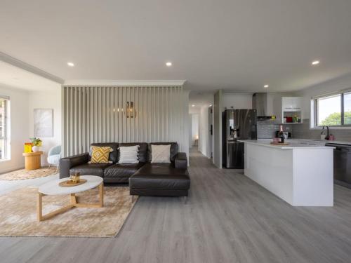 a living room with a black couch and a kitchen at Convenient Comfort 4BR near Malls and Transport in Brisbane