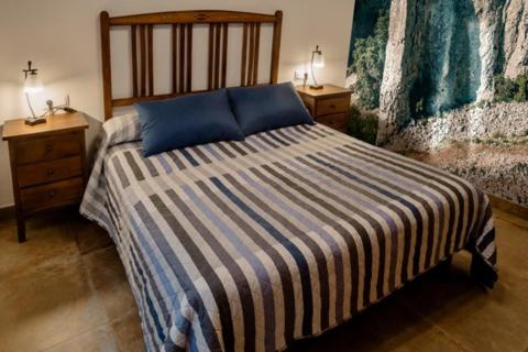 a bedroom with a bed with a striped blanket and two night stands at Ca iaia Rosario - Casa rural con catas premiadas, obrador y senderismo in Cuatretondeta
