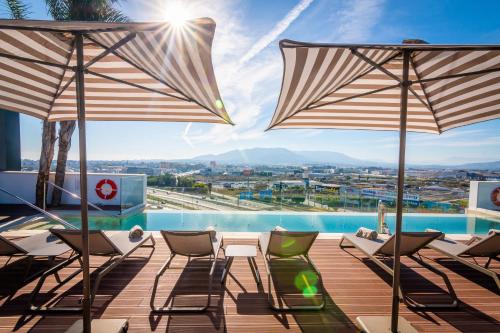 eine Terrasse mit Stühlen, Sonnenschirmen und einem Pool in der Unterkunft Hotel Málaga Vibes in Málaga