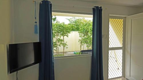 a window with blue curtains and a television in a room at Ciri's Apartelle in Moalboal