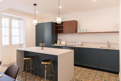 a kitchen with black cabinets and a white counter and stools at Florette Suite Designer Finish with Stunning Lounge Terrace by ArcoBnb in Il-Furjana