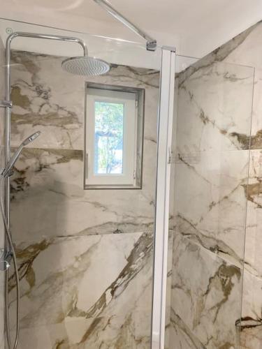 La salle de bains est pourvue d'un mur en marbre et d'une fenêtre. dans l'établissement Maison à 150m de la plage naturiste, 2 chambres, à Linguizzetta