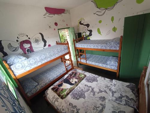 a room with three bunk beds and a wall with drawings at Sumé Hostel in São Thomé das Letras