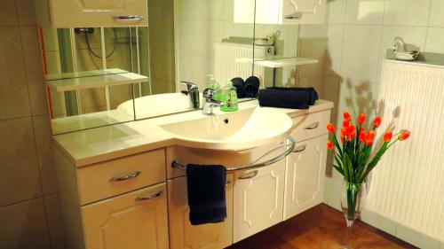 uma casa de banho com lavatório, espelho e flores em Wellness Apartments Sophienhöhe AM TEICH em Mechernich