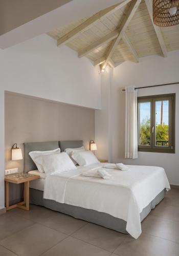 a white bedroom with a large bed and a window at Callisto Seaside Homes & Suites in Marathopolis