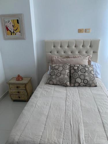 1 cama con colcha blanca y almohadas en Apartamento Cerca Al Hotel Las Américas, en Cartagena de Indias