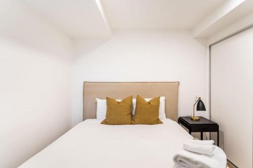 een witte slaapkamer met een bed met gele kussens bij City Fringe Crash Pad in Auckland