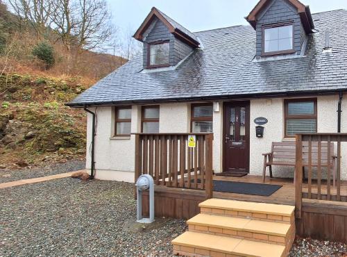 una casa con un porche de madera con un banco. en Ben Vorlich Cottage, en Tarbet