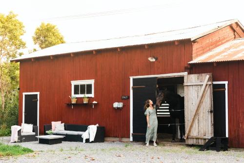 a woman standing in the doorway of a red barn with a horse at Glamping in Småland in Eksjö