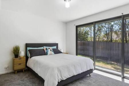 Dormitorio blanco con cama y ventana grande en New Architect designed Coastal retreat-water views en Hobart