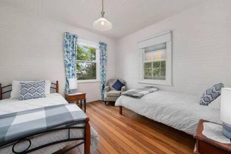 a bedroom with two beds and a chair and two windows at The Baker's Cottage in the Heart of Richmond Sleeps 6 in Hobart