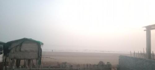 a foggy field with a farm in the background at Ocean front beach resort in Tajpur