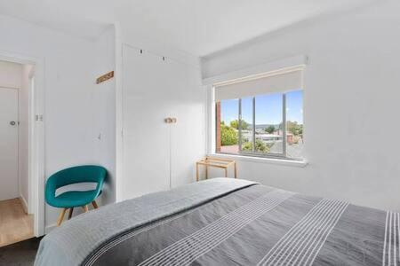 een witte slaapkamer met een bed en een raam bij Renovated unit in leafy surrounds close to shops in Hobart